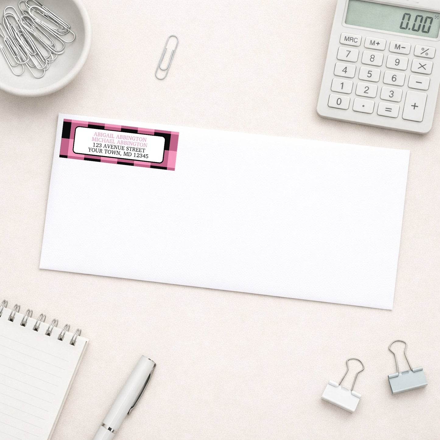 Light Pink and Black Buffalo Plaid Address Label shown on a white envelope with everyday office supplies