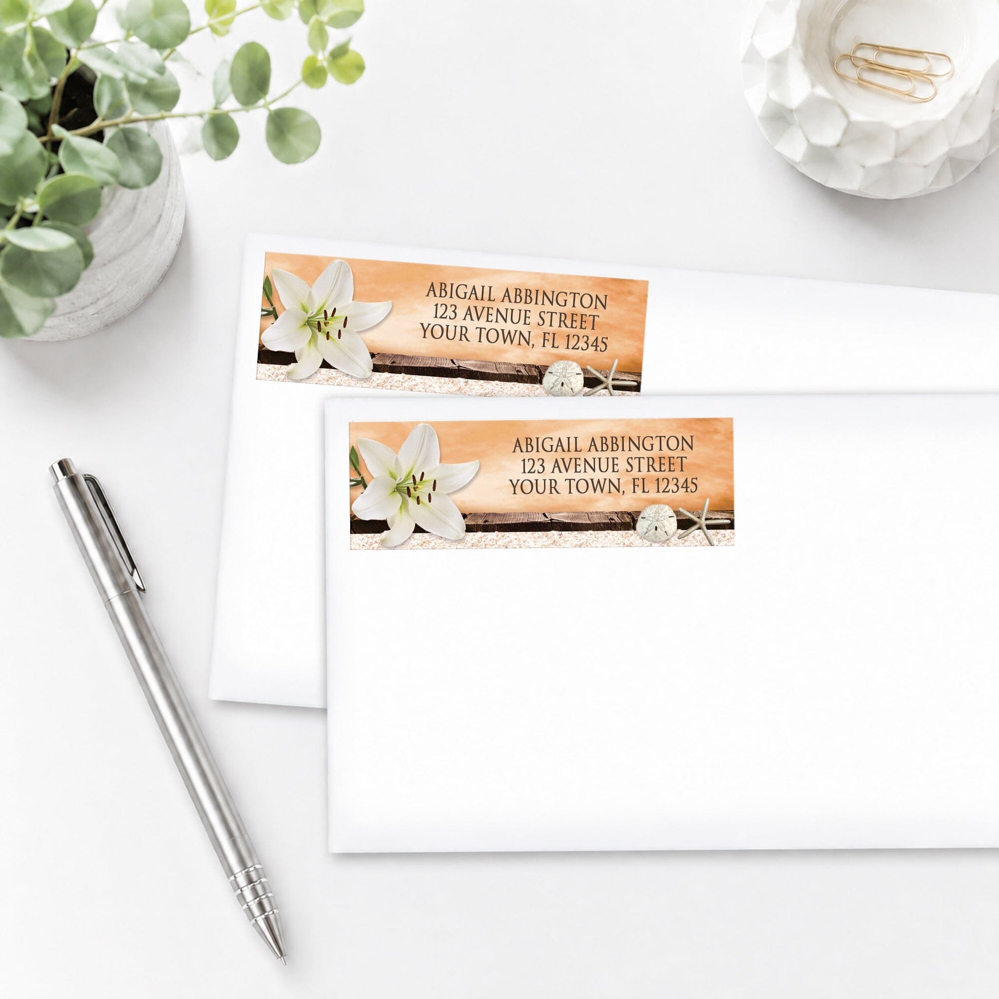 Lily Seashells and Sand Autumn Beach Address Labels on white envelopes next to a pen and plant on a white surface.