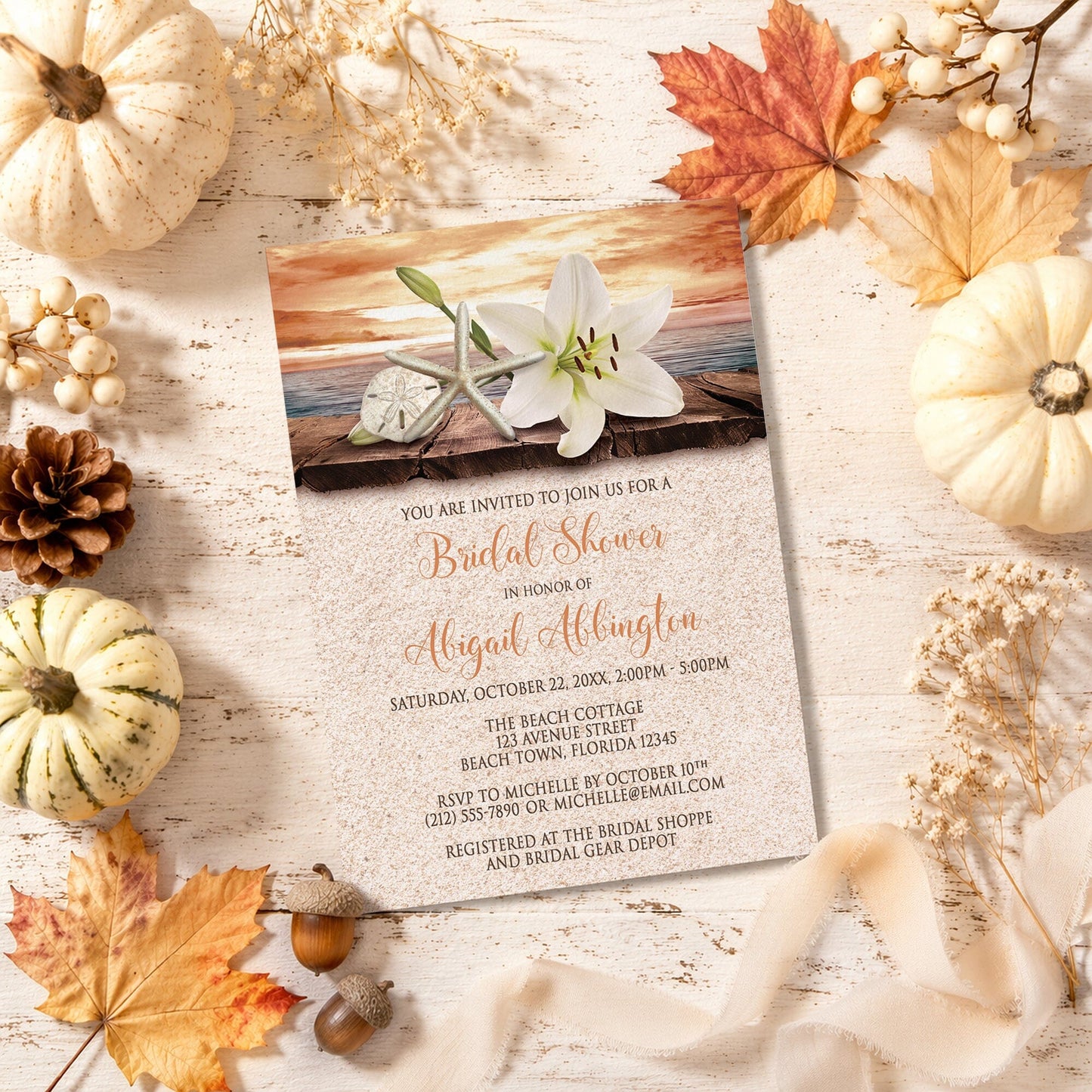 Lily Seashells and Sand Autumn Beach Bridal Shower Invitation with autumn decorations on a wooden surface