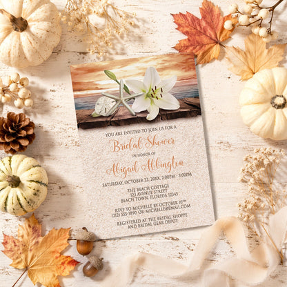 Lily Seashells and Sand Autumn Beach Bridal Shower Invitation with autumn decorations on a wooden surface