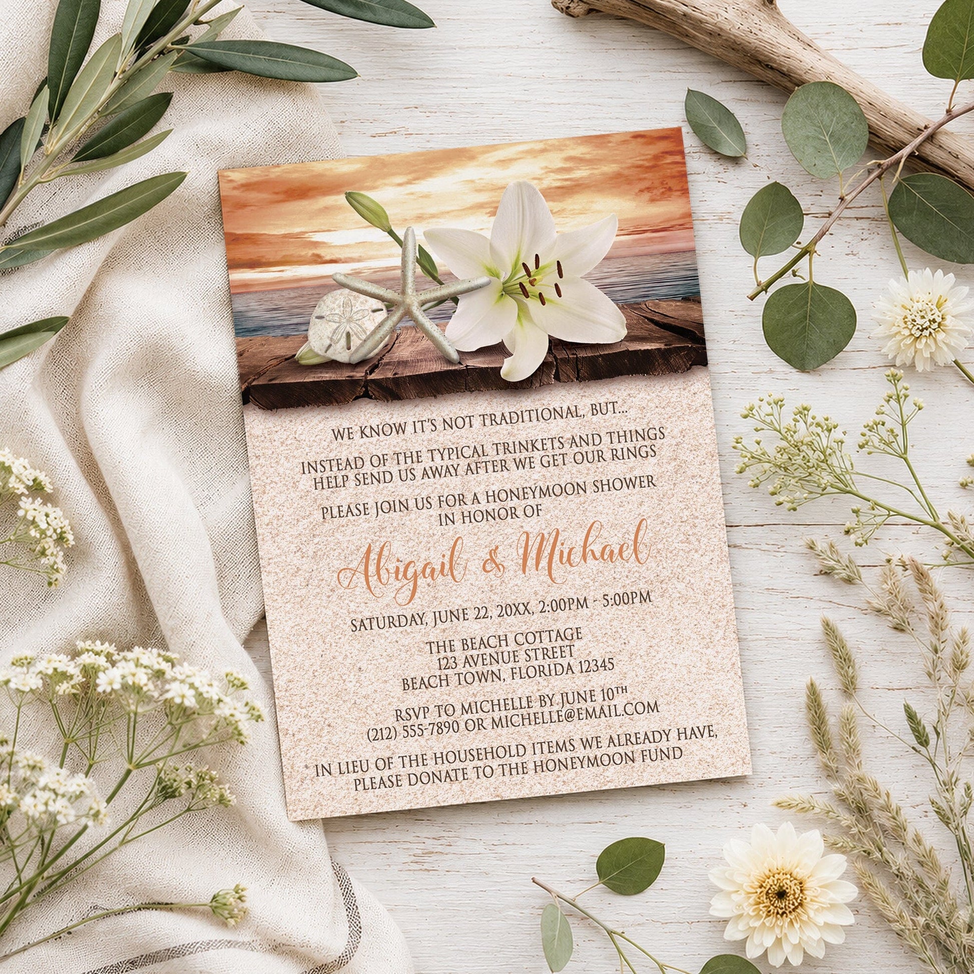 Lily Seashells and Sand Autumn Beach Honeymoon Shower Invitation shown on a light wooden surface with summer plants.