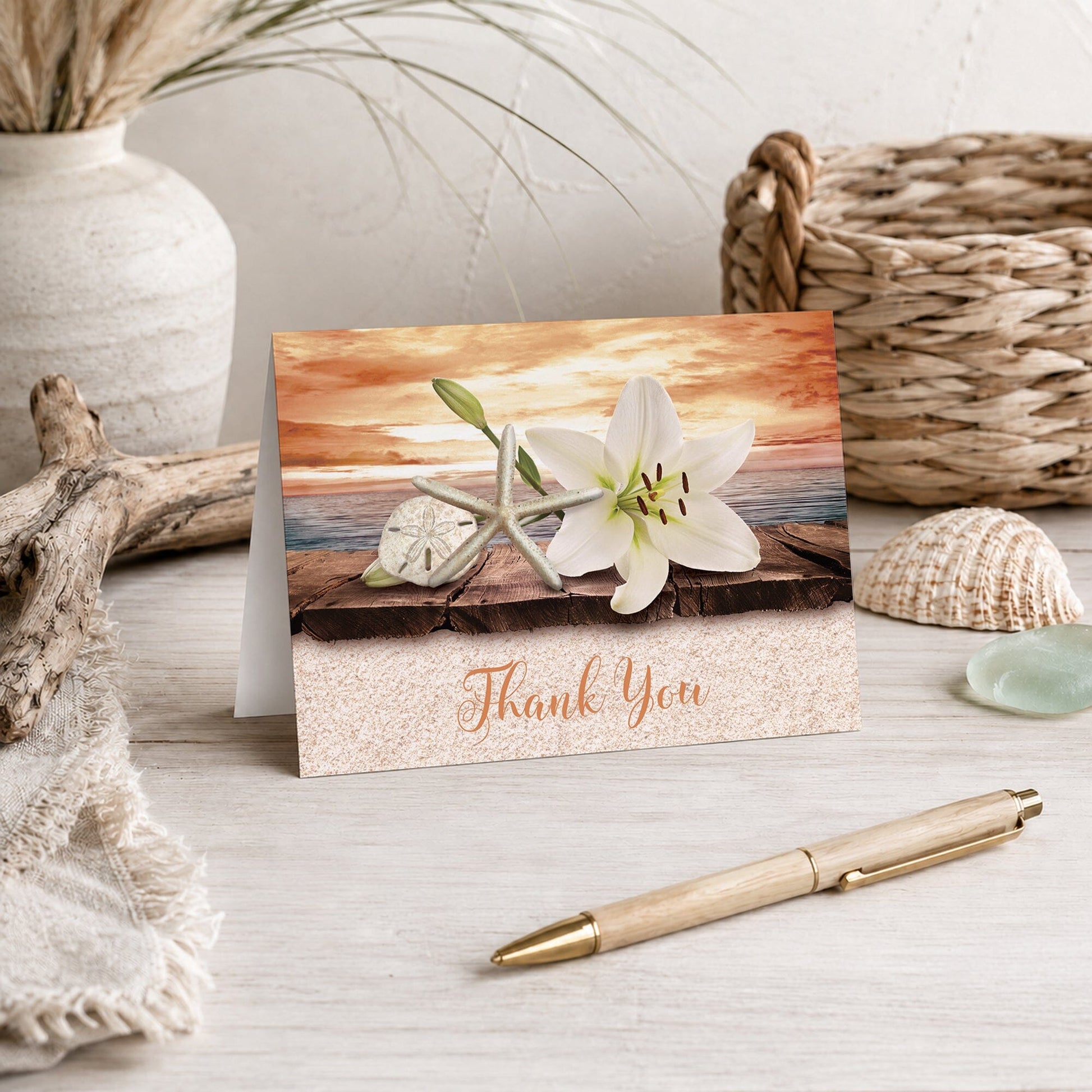 Lily Seashells and Sand Autumn Beach Thank You Card shown on a beach house tabletop with coastal decor and a pen.