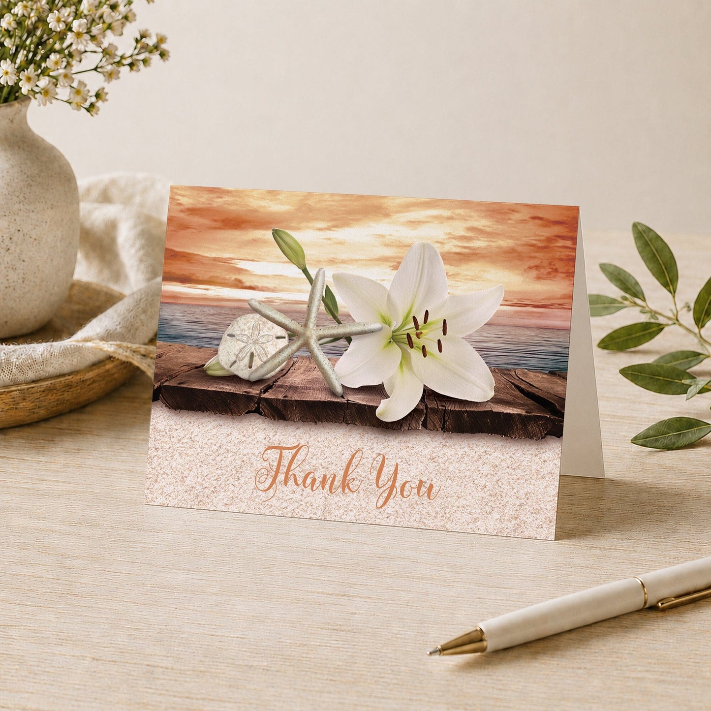 Lily Seashells and Sand Autumn Beach Thank You Card shown on a desk with a vase, plants, and a pen.