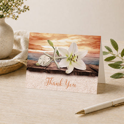 Lily Seashells and Sand Autumn Beach Thank You Card shown on a desk with a vase, plants, and a pen.