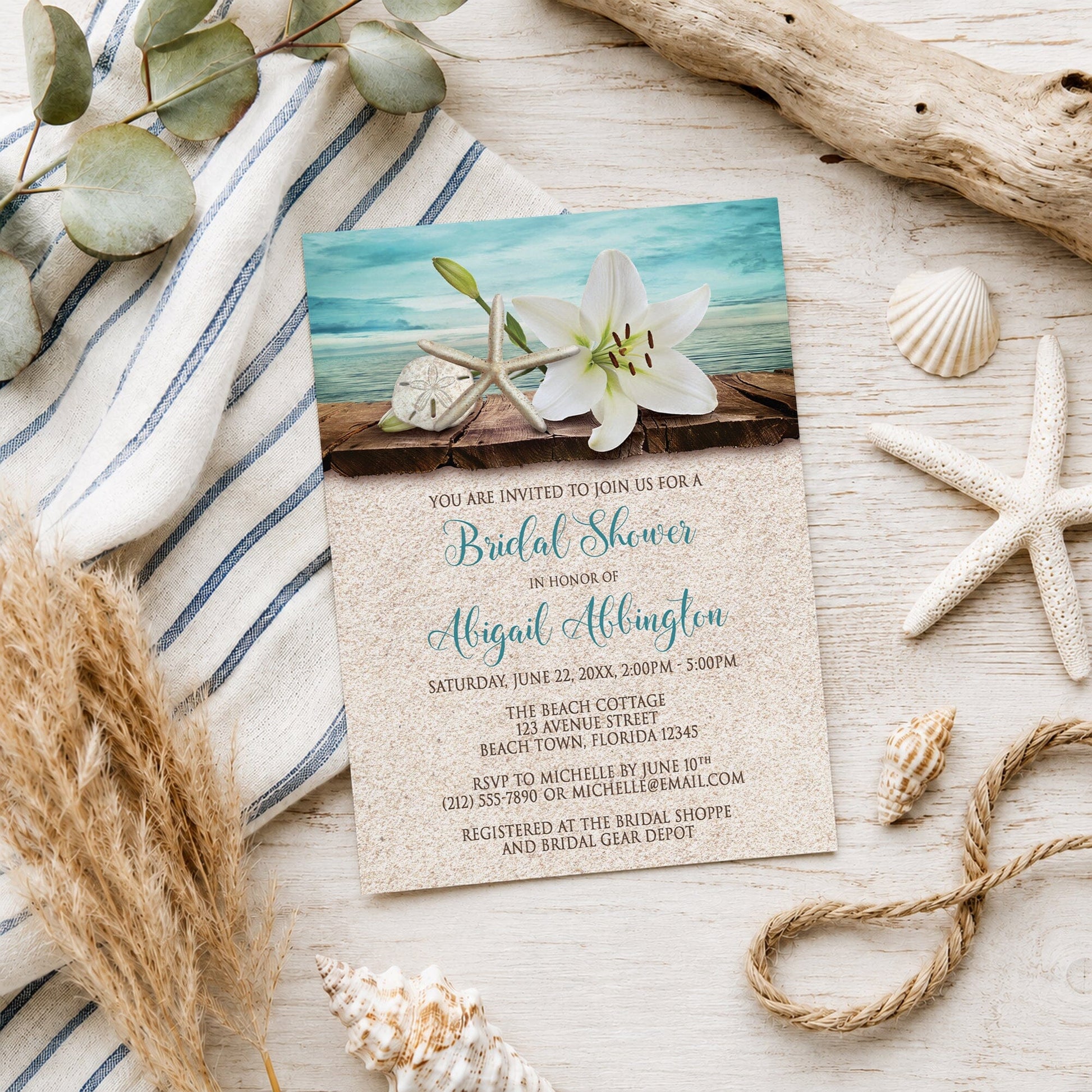 Lily Seashells and Sand Beach Bridal Shower Invitation shown on a light wooden surface with seashells and coastal decor.