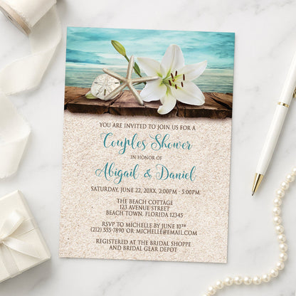Lily Seashells and Sand Beach Couples Shower Invitation shown on a marble surface with a white gift box, pen, ribbon, and pearls.