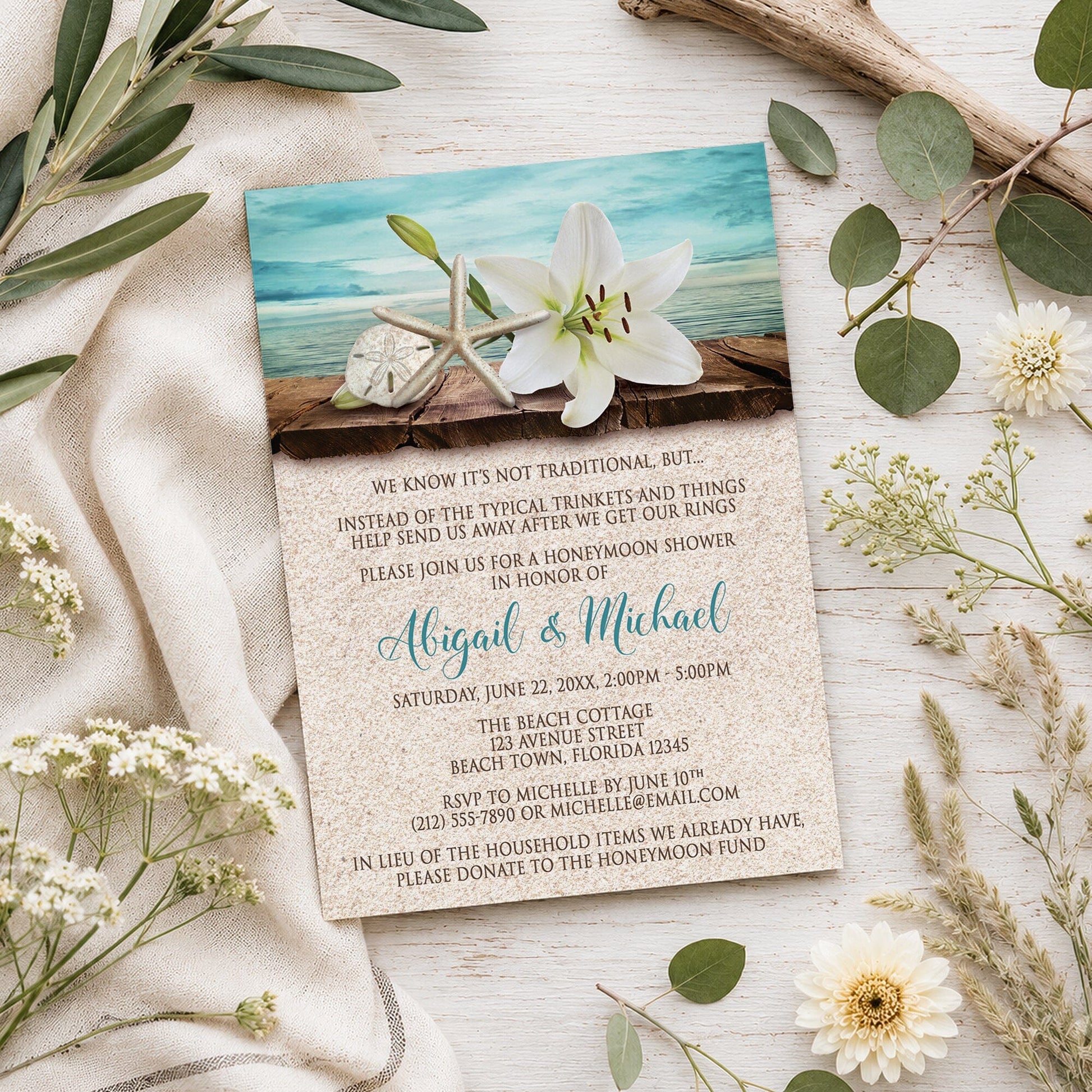 Lily Seashells and Sand Beach Honeymoon Shower Invitation shown on a light wooden surface with summer plants.