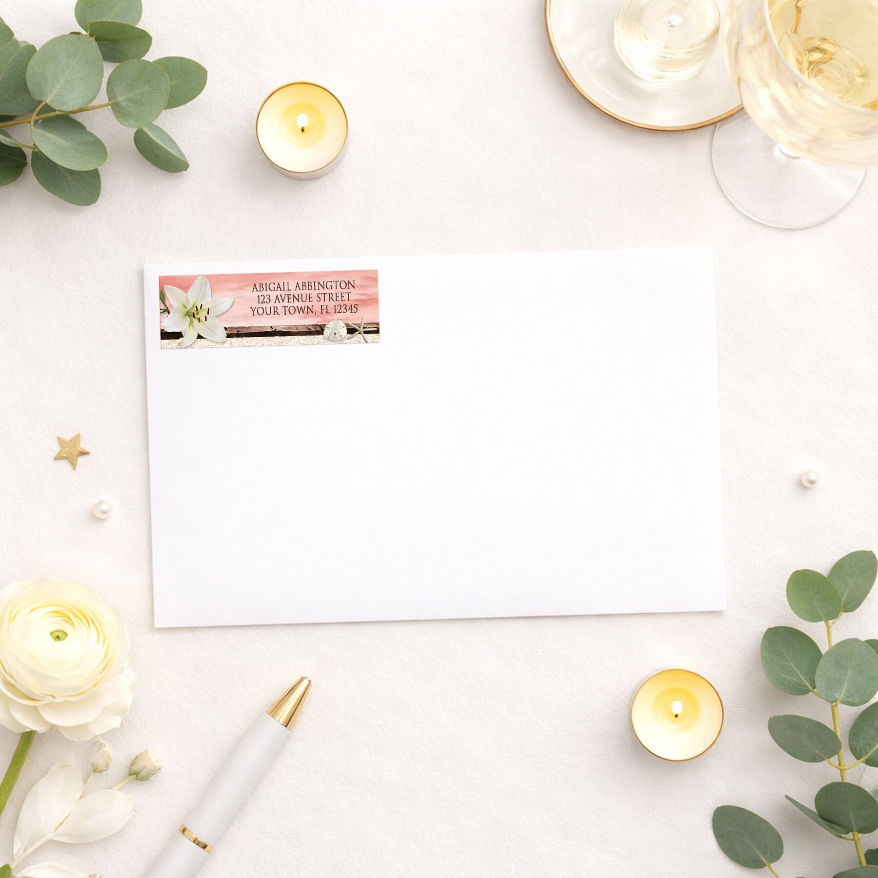 Lily Seashells and Sand Coral Beach Address Label shown on a white envelope with wedding and shower supplies