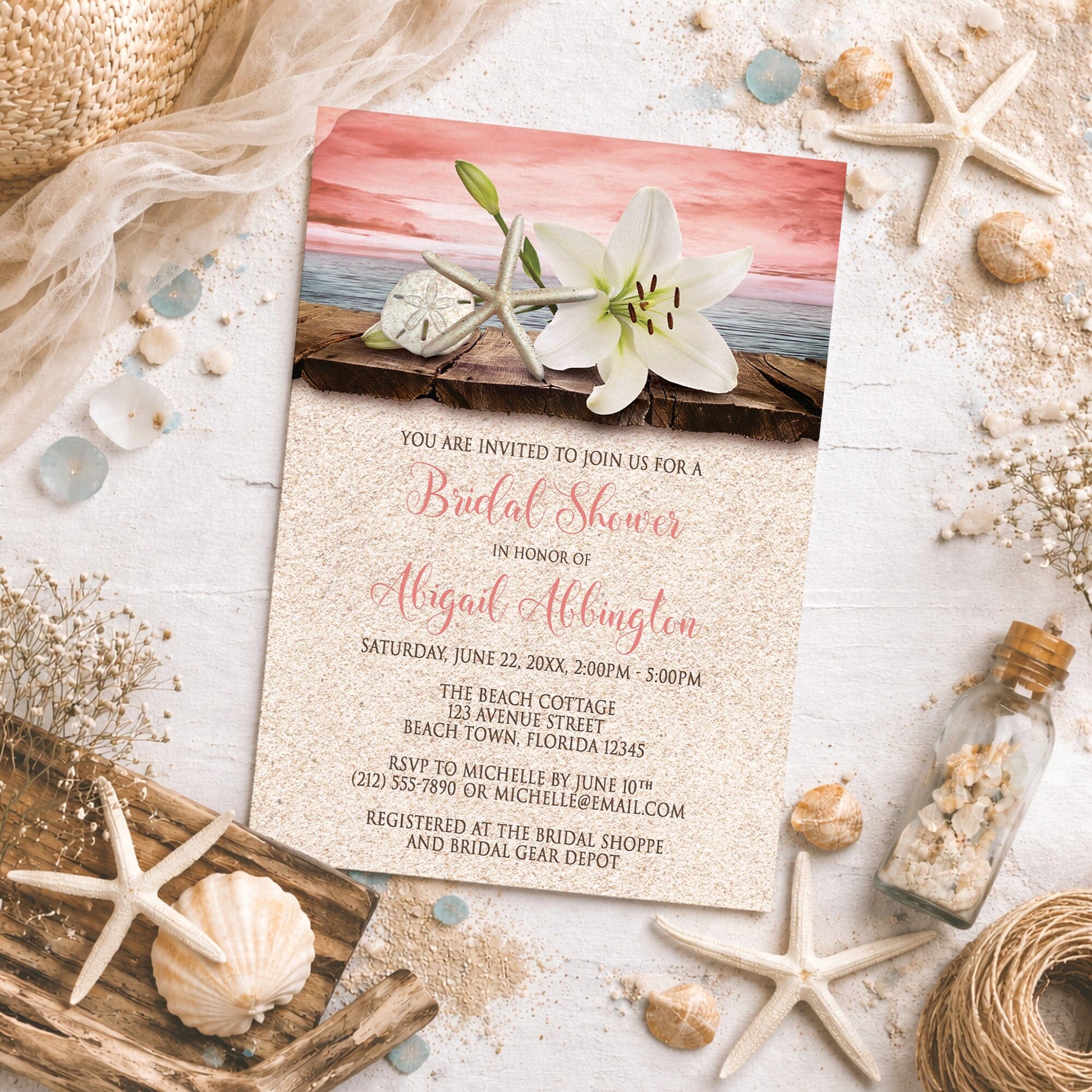 Lily Seashells and Sand Coral Beach Bridal Shower Invitation on a rough surface with seashells, drift wood, sand, and other beach decor.