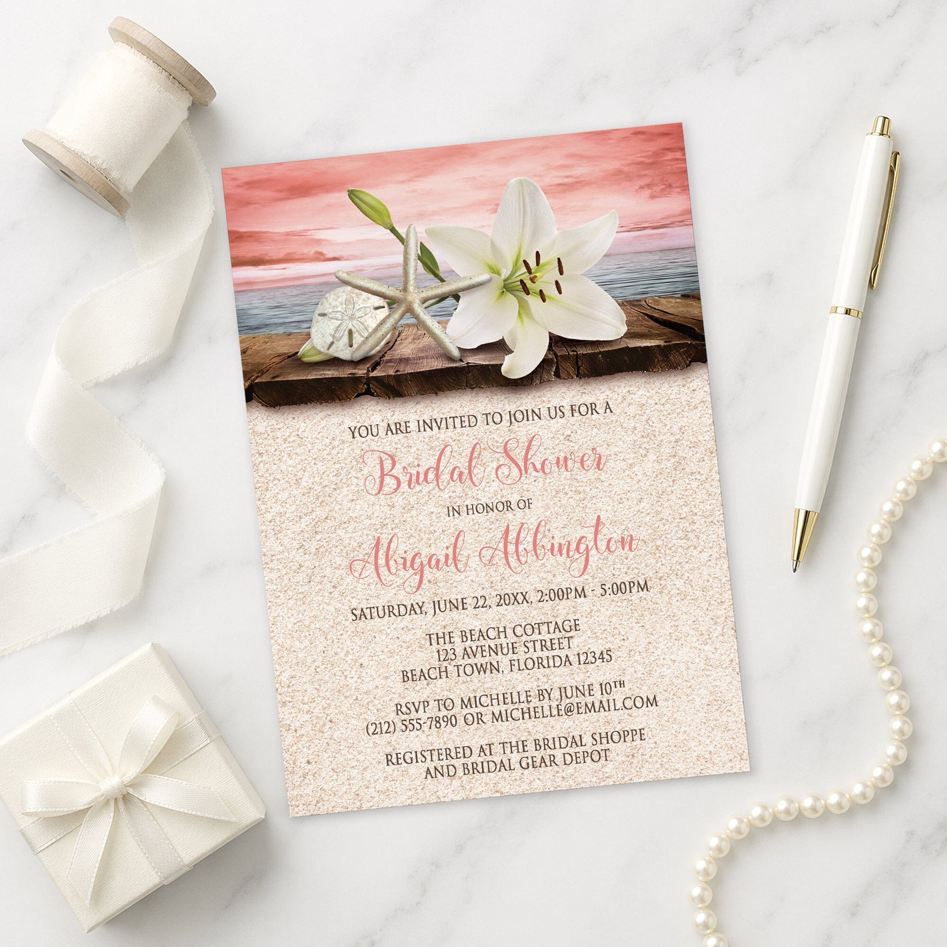 Lily Seashells and Sand Coral Beach Bridal Shower Invitation on a marble surface with ribbon and pen.