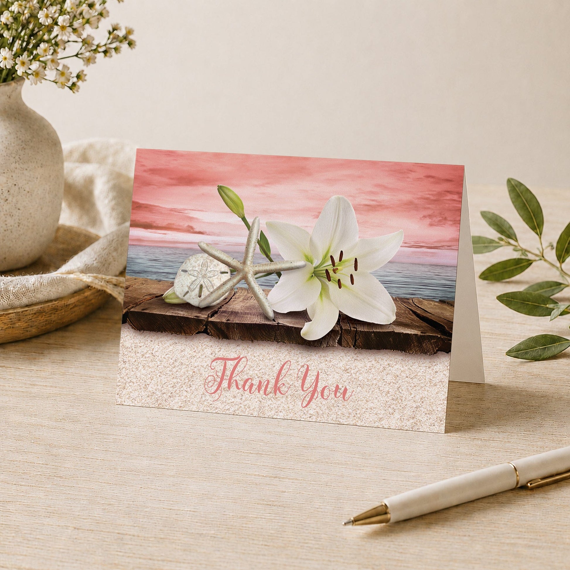 Lily Seashells and Sand Coral Beach Thank You Card shown on a tabletop with a vase, plants, and a pen.