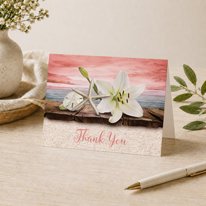 Lily Seashells and Sand Coral Beach Thank You Card shown on a tabletop with a vase, plants, and a pen.