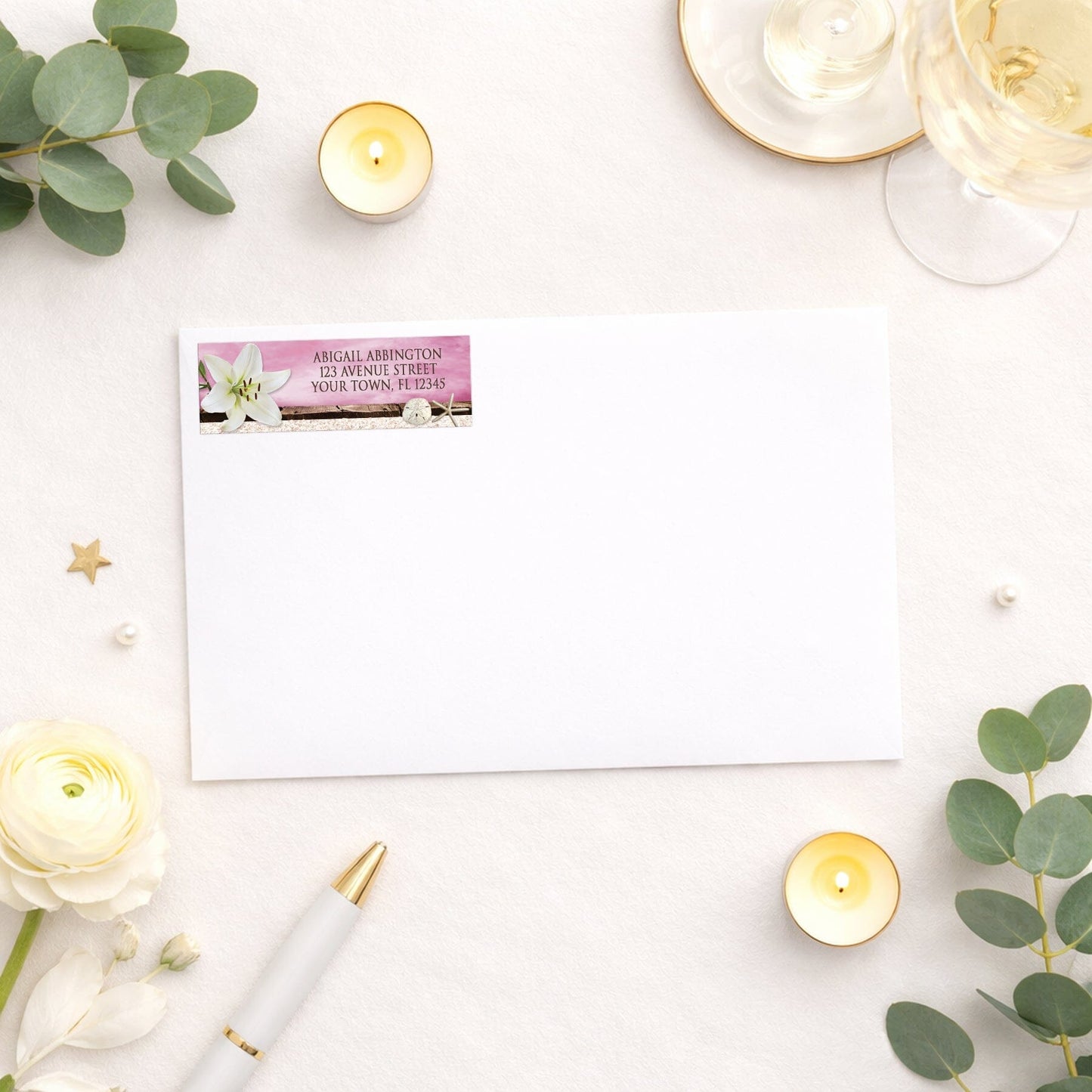 Lily Seashells and Sand Magenta Beach Address Label shown on a white envelope with wedding and shower supplies
