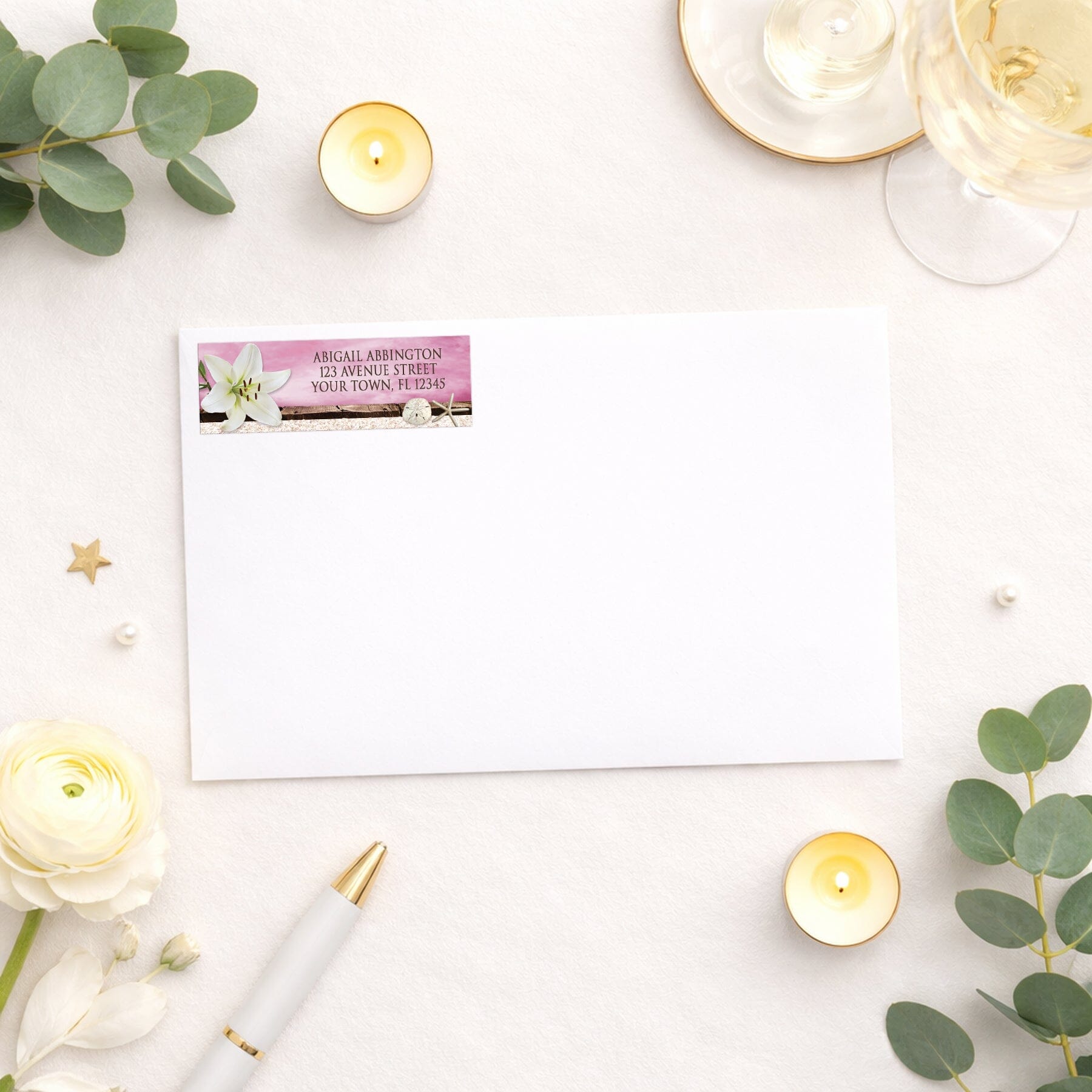 Lily Seashells and Sand Magenta Beach Address Label shown on a white envelope with wedding and shower supplies