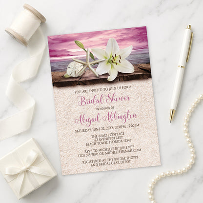 Lily Seashells and Sand Magenta Beach Bridal Shower Invitation on a marble surface with a white gift box, pen, ribbon, and pearls.