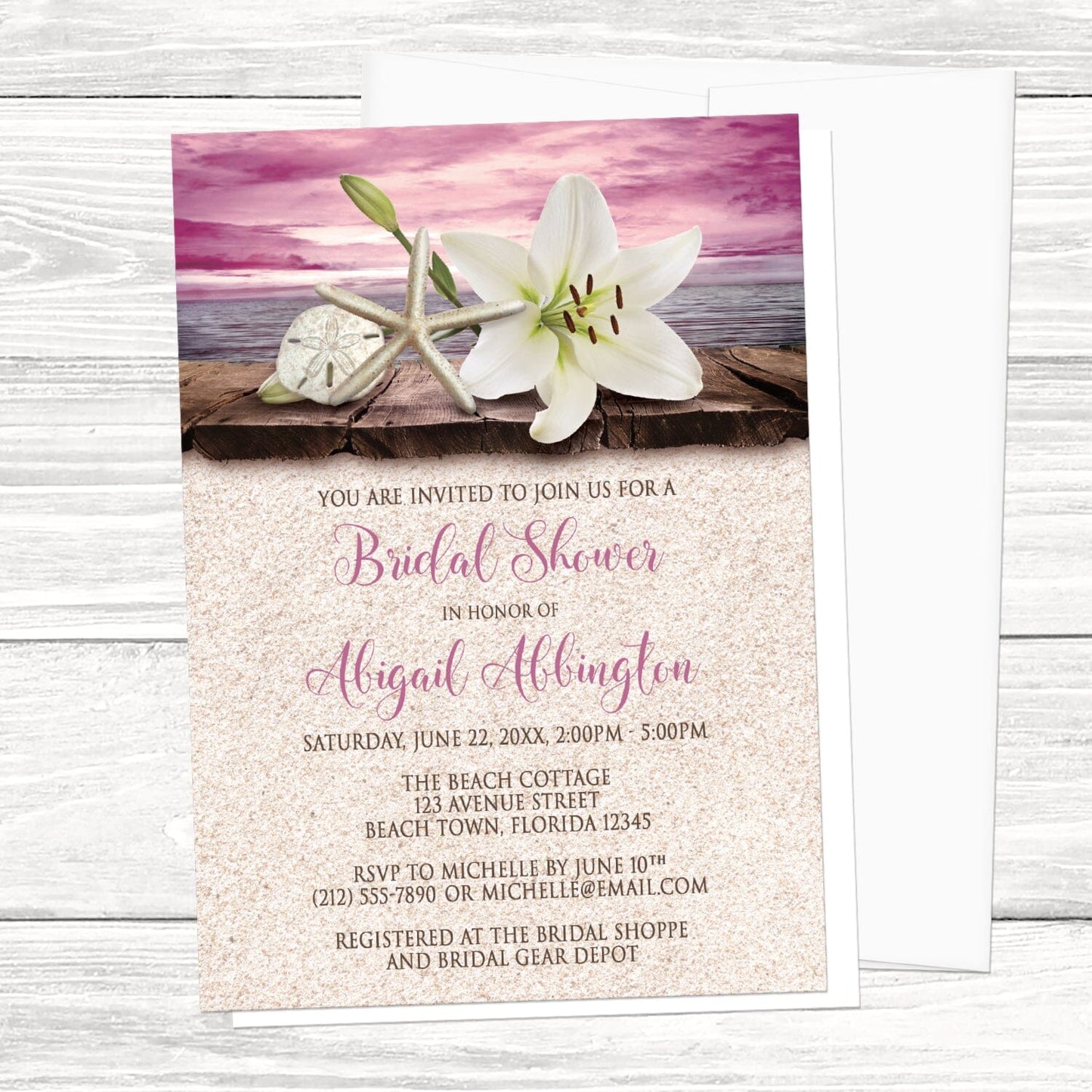 Lily Seashells and Sand Magenta Beach Bridal Shower Invitation shown on a light wood surface with a white envelope.