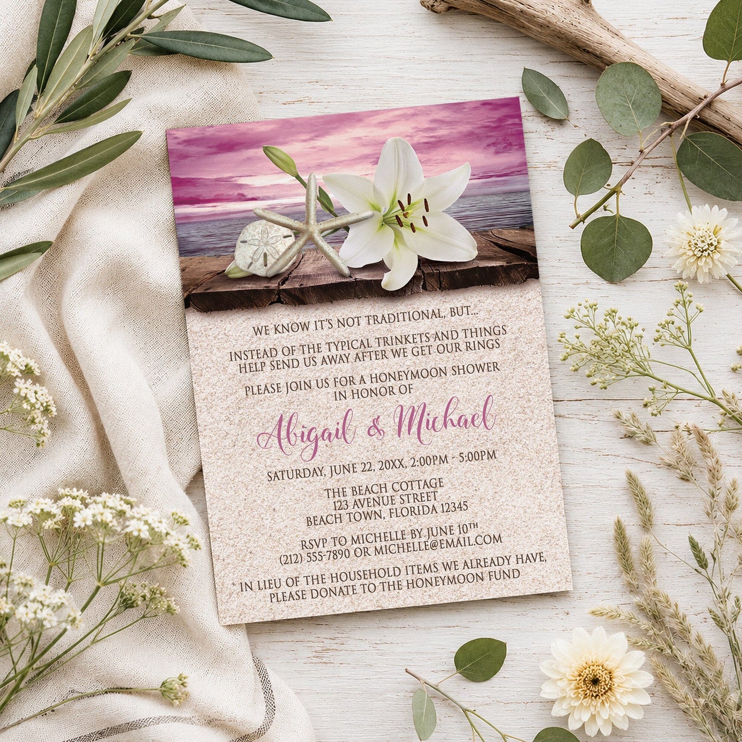 Lily Seashells and Sand Magenta Beach Honeymoon Shower Invitation shown on a wooden surface with summer plants.