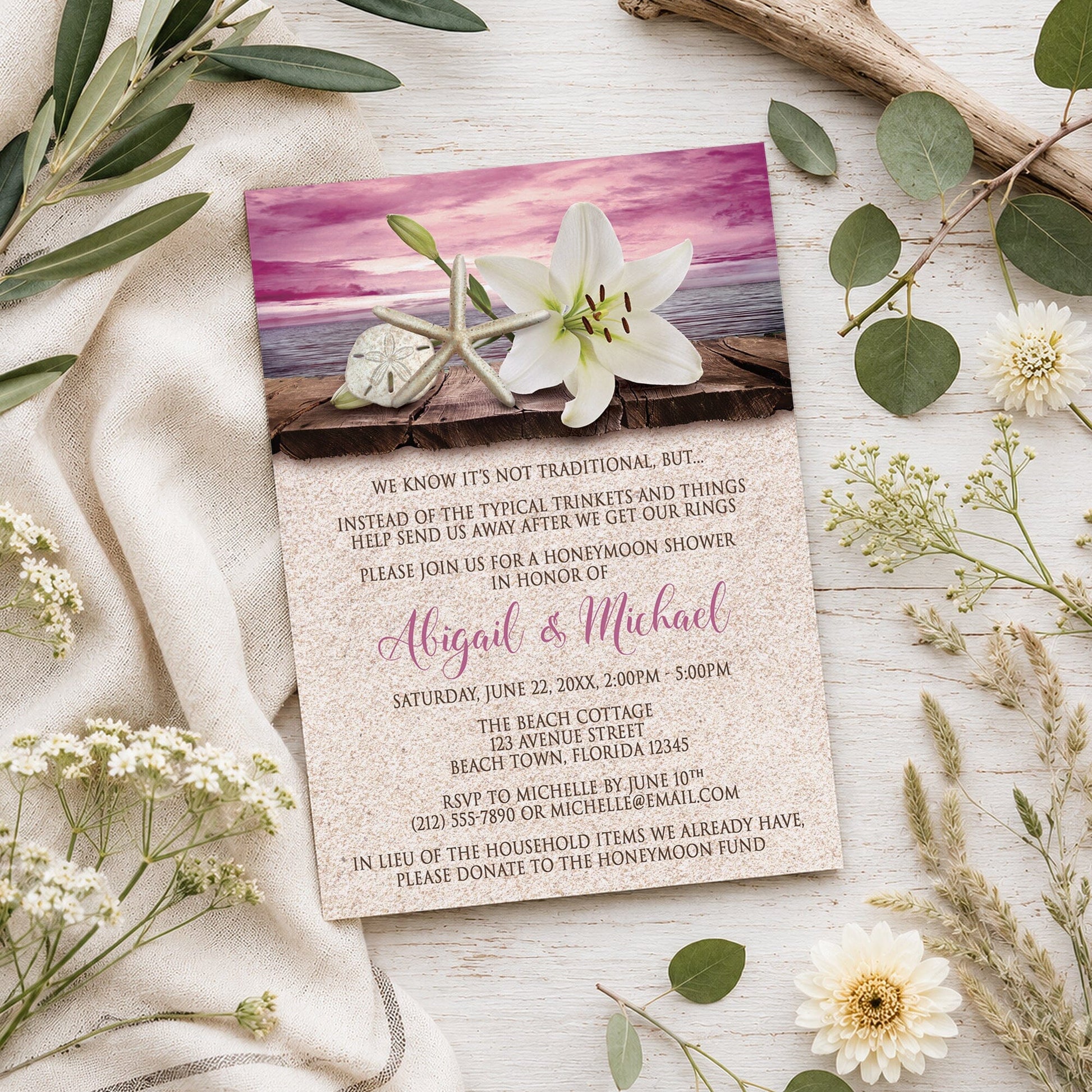Lily Seashells and Sand Magenta Beach Honeymoon Shower Invitation shown on a wooden surface with summer plants.