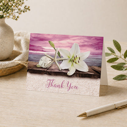 Lily Seashells and Sand Magenta Beach Thank You Card shown on a desk with a vase, plants, and a pen.