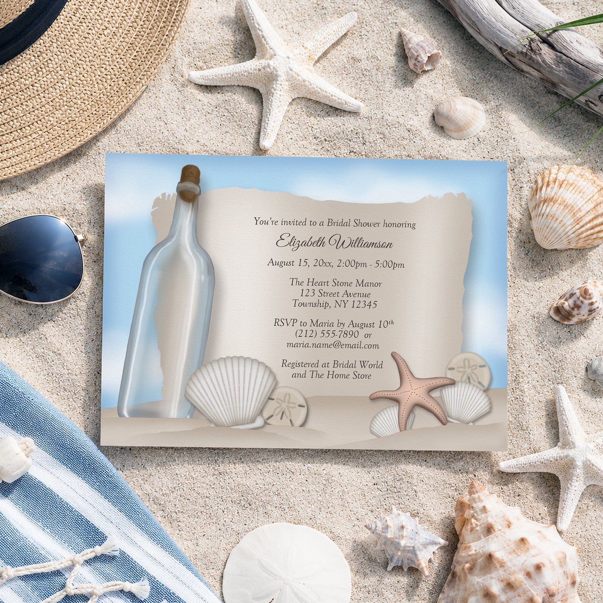 Message from a Bottle Beach Bridal Shower Invitation shown on sand with seashells and other beach accessories.