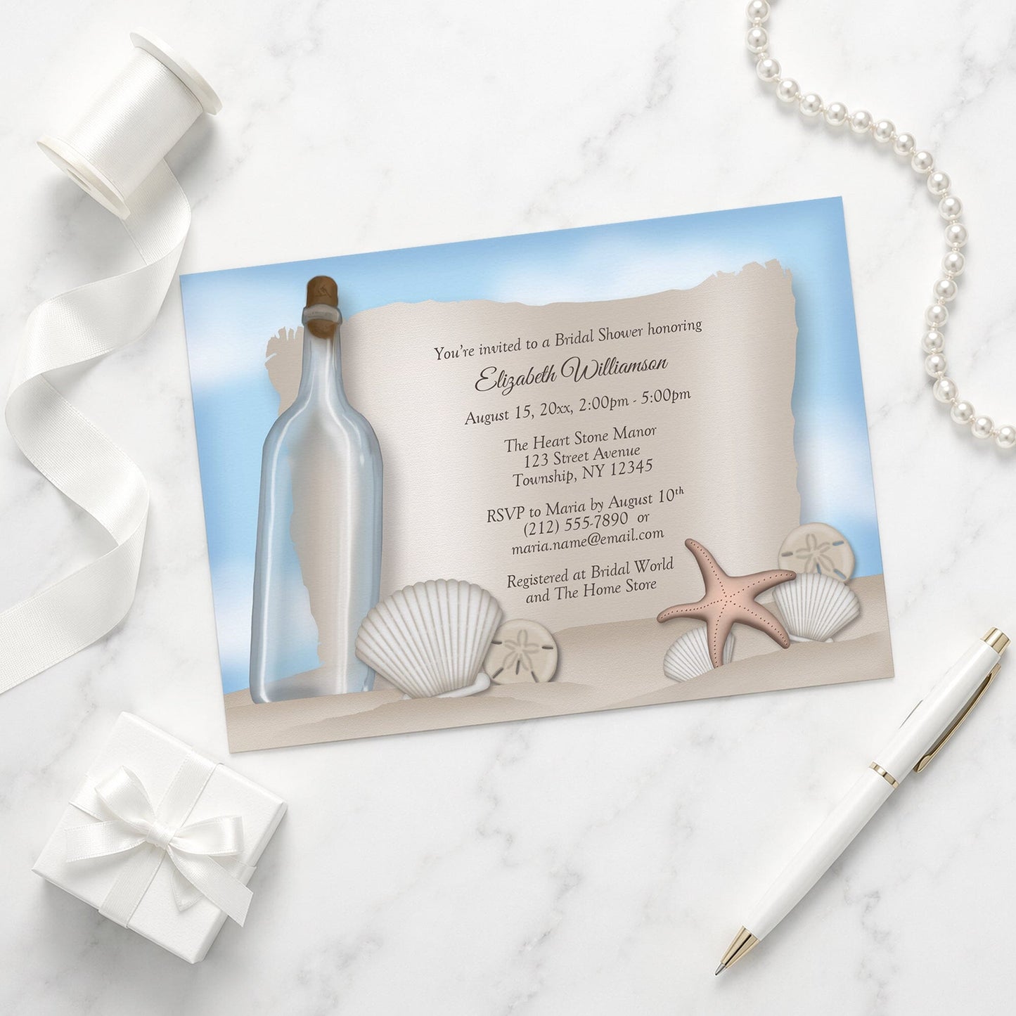 Seashell-themed Message from a Bottle Beach Bridal Shower Invitation on a marble surface with a gift box and pen.