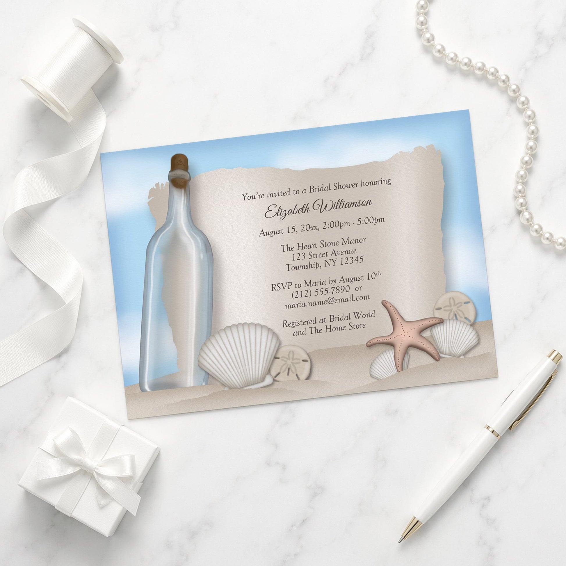 Seashell-themed Message from a Bottle Beach Bridal Shower Invitation on a marble surface with a gift box and pen.