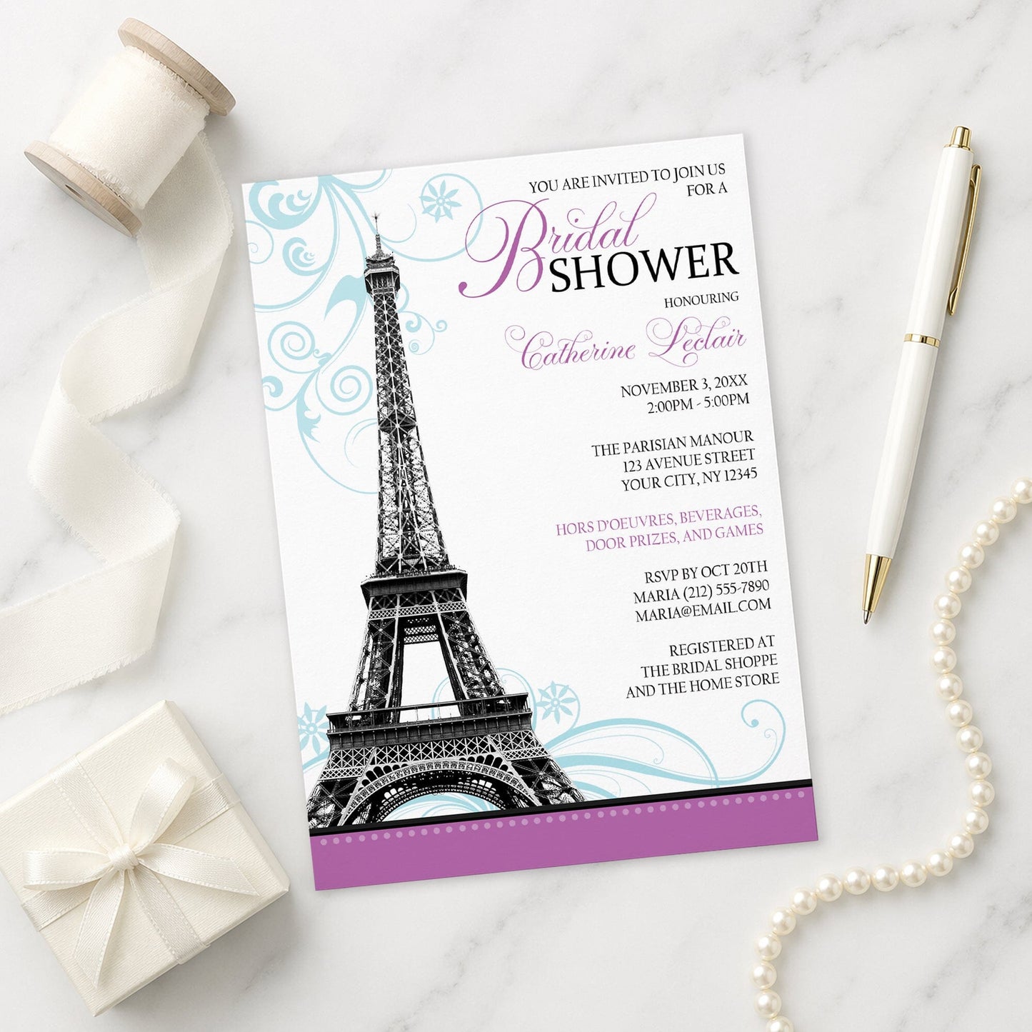 Modern Eiffel Tower Purple Parisian Bridal Shower Invitation shown on a marble surface with a white gift box, pen, ribbon, and pearls.