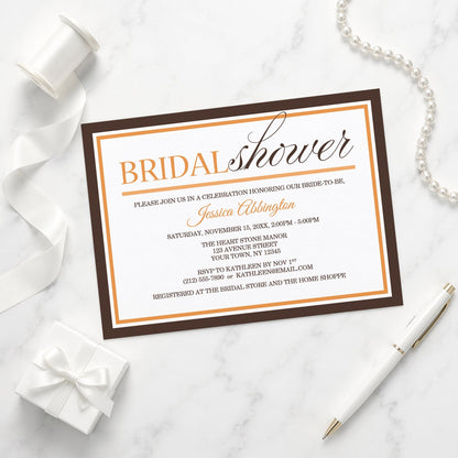 Modern Orange and Brown Autumn Bridal Shower Invitation shown on a marble surface with a white gift box, pen, ribbon, and pearls.