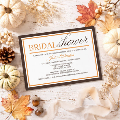 Modern Orange and Brown Autumn Bridal Shower Invitation shown on a rustic surface with fall leaves and autumn decor.