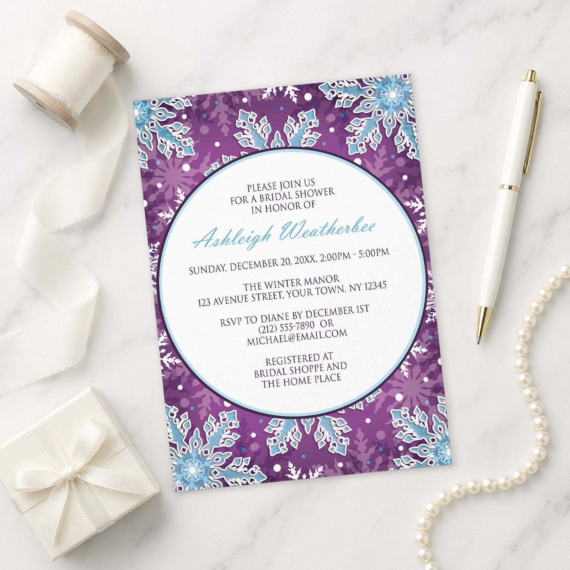 Modern Purple Blue Snowflake Bridal Shower Invitation shown on a marble surface with a white gift box, pen, ribbon, and pearls.