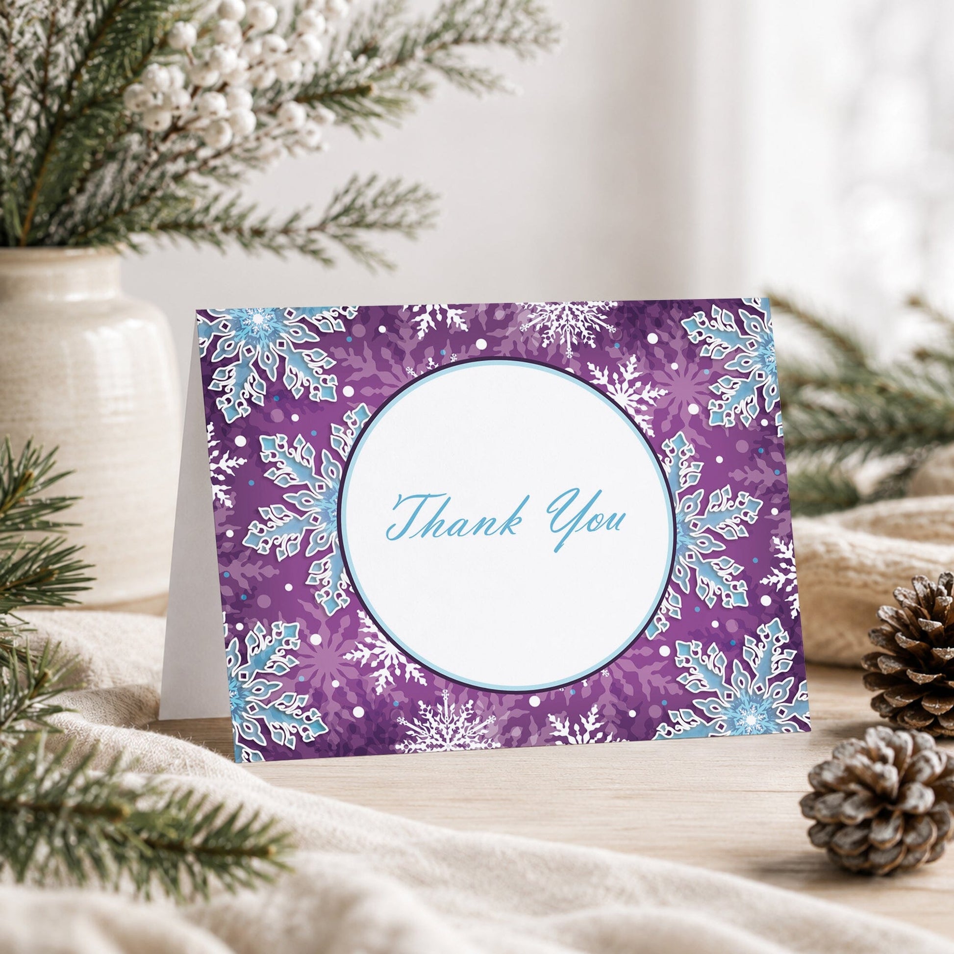 Modern Purple Blue Snowflake Thank You Card shown on a tabletop with a vase, winter greenery, and pine cones.