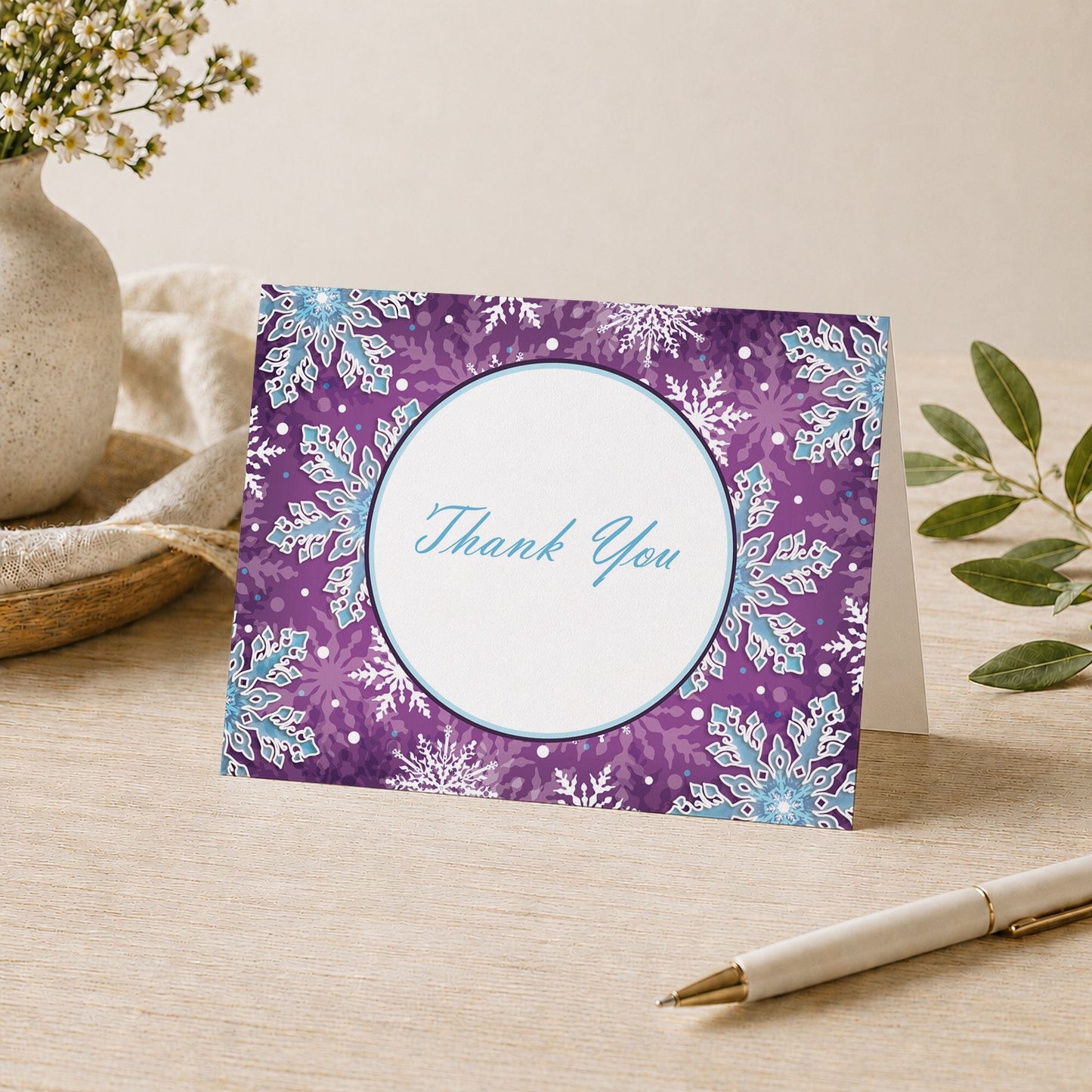 Modern Purple Blue Snowflake Thank You Card shown on a desk with a vase, plants, and a pen.