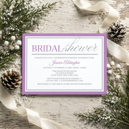 Modern Purple and Gray Bridal Shower Invitation shown on a rustic surface with winter greenery, pine cones, and ribbons.