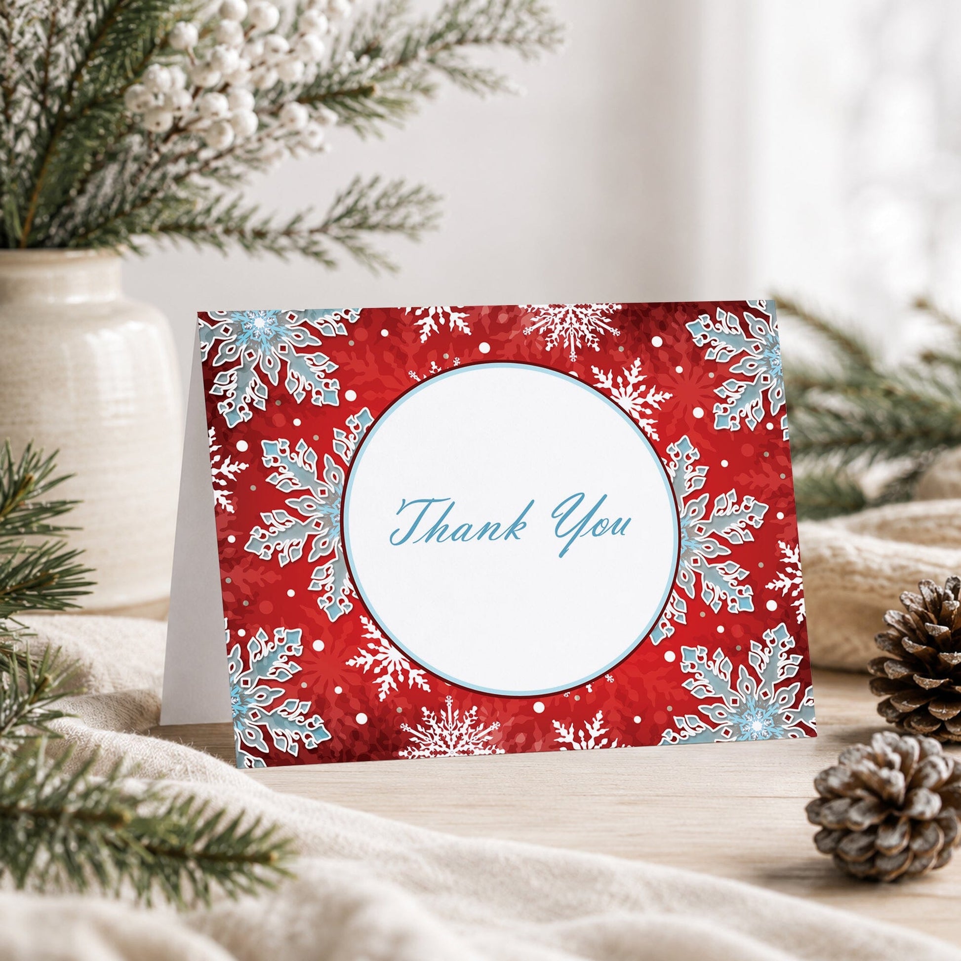 Modern Red White Blue Snowflake Thank You Card shown on a tabletop with a vase, winter greenery, and pine cones.