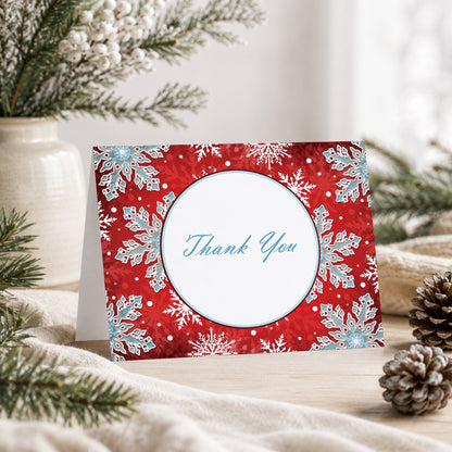 Modern Red White Blue Snowflake Thank You Card shown on a tabletop with a vase, winter greenery, and pine cones.
