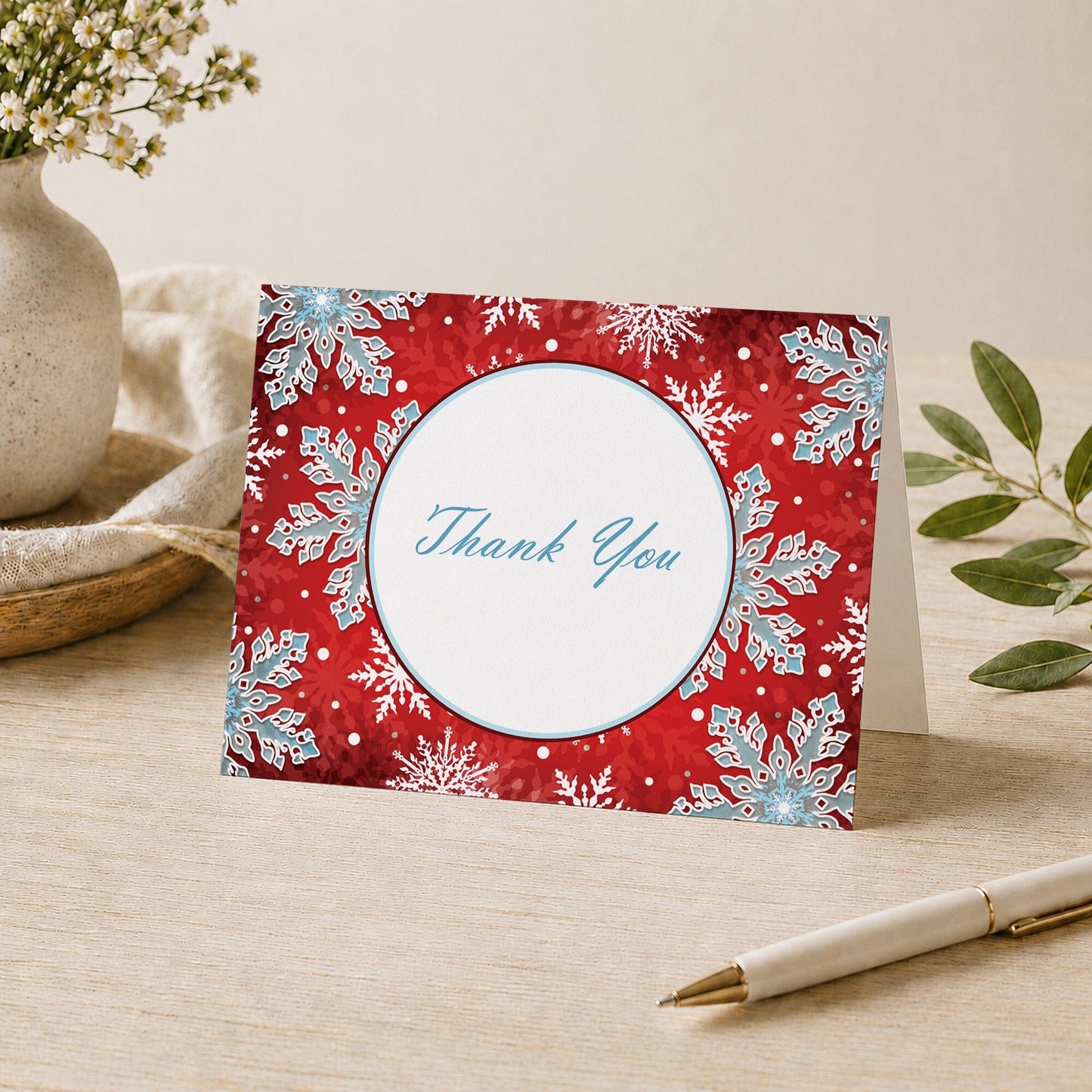Modern Red White Blue Snowflake Thank You Card shown on a desk with a vase, plants, and a pen.