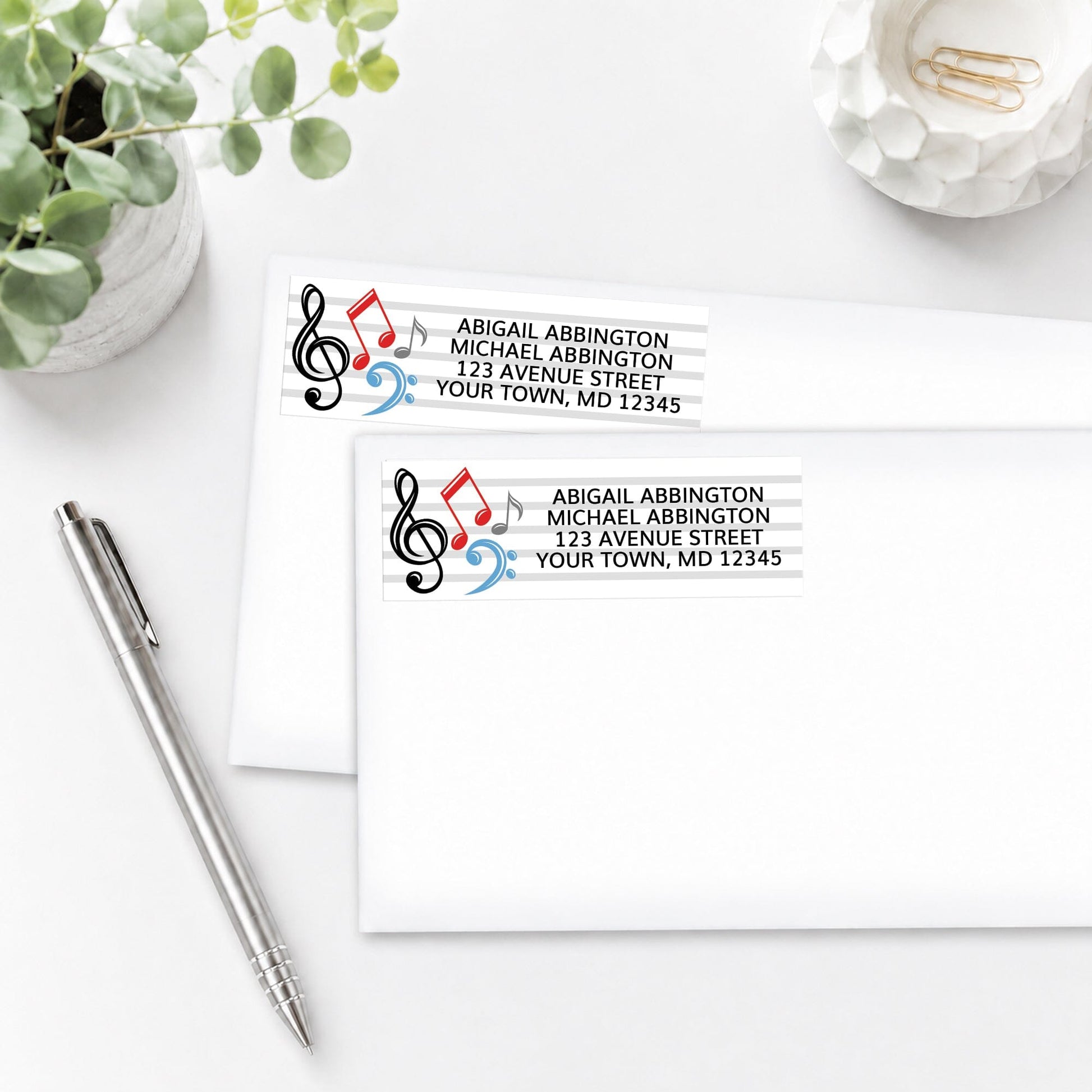 Music Notes Address Labels shown on white envelopes on a white surface with plants and a pen.