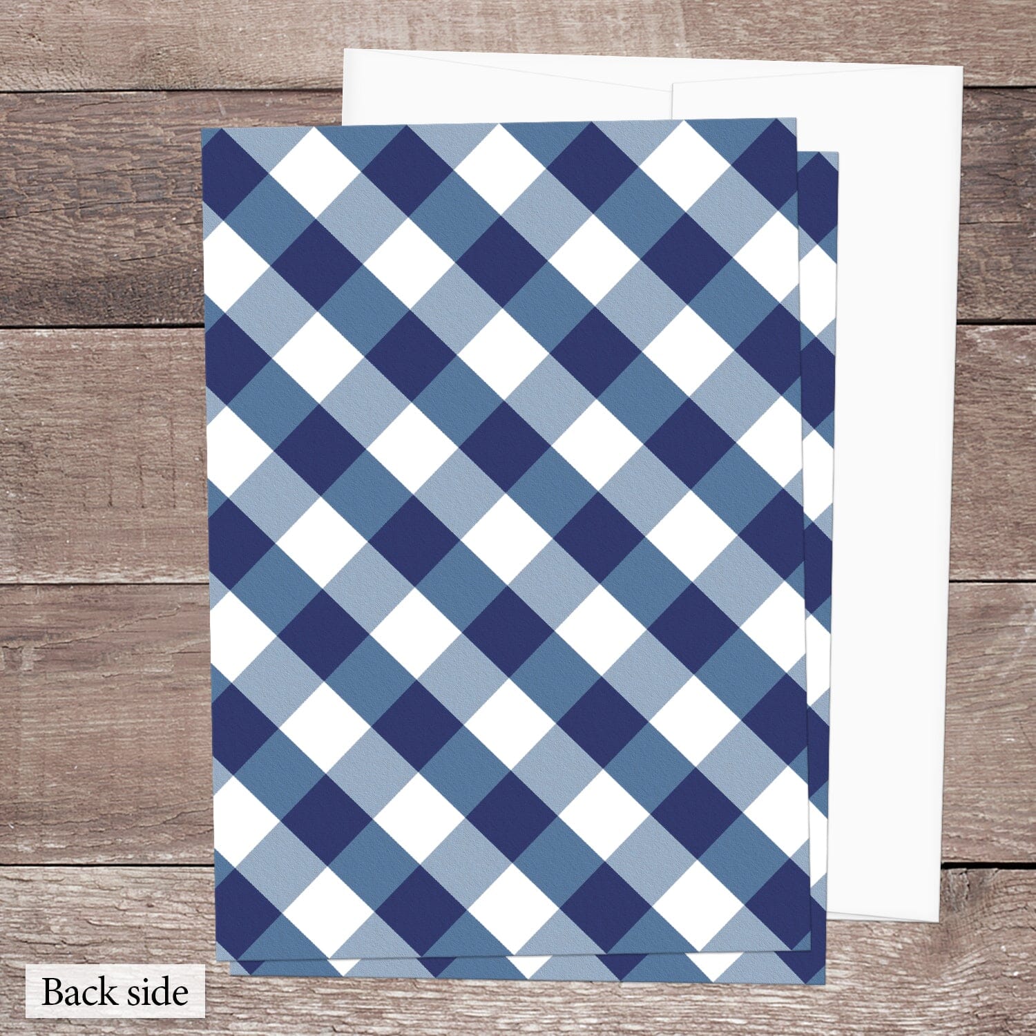 Back side of the printed Navy Blue Gingham Vow Renewal Invitations featuring the diagonal blue and white check pattern, shown on a brown wood surface with a white envelope.