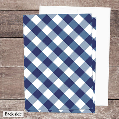 Back side of the printed Navy Blue Gingham Vow Renewal Invitations featuring the diagonal blue and white check pattern, shown on a brown wood surface with a white envelope.