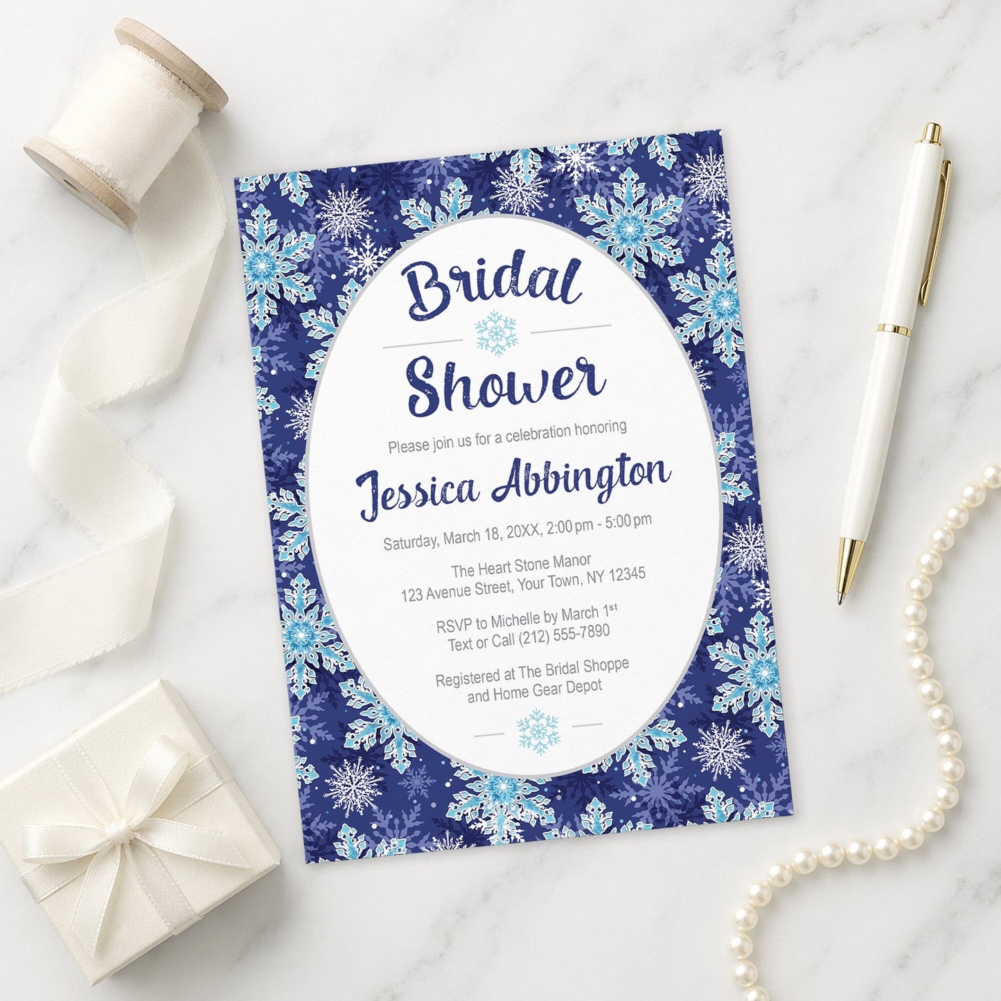 Navy Blue Snowflake Bridal Shower Invitation on a marble surface with gift, pen, and pearls.