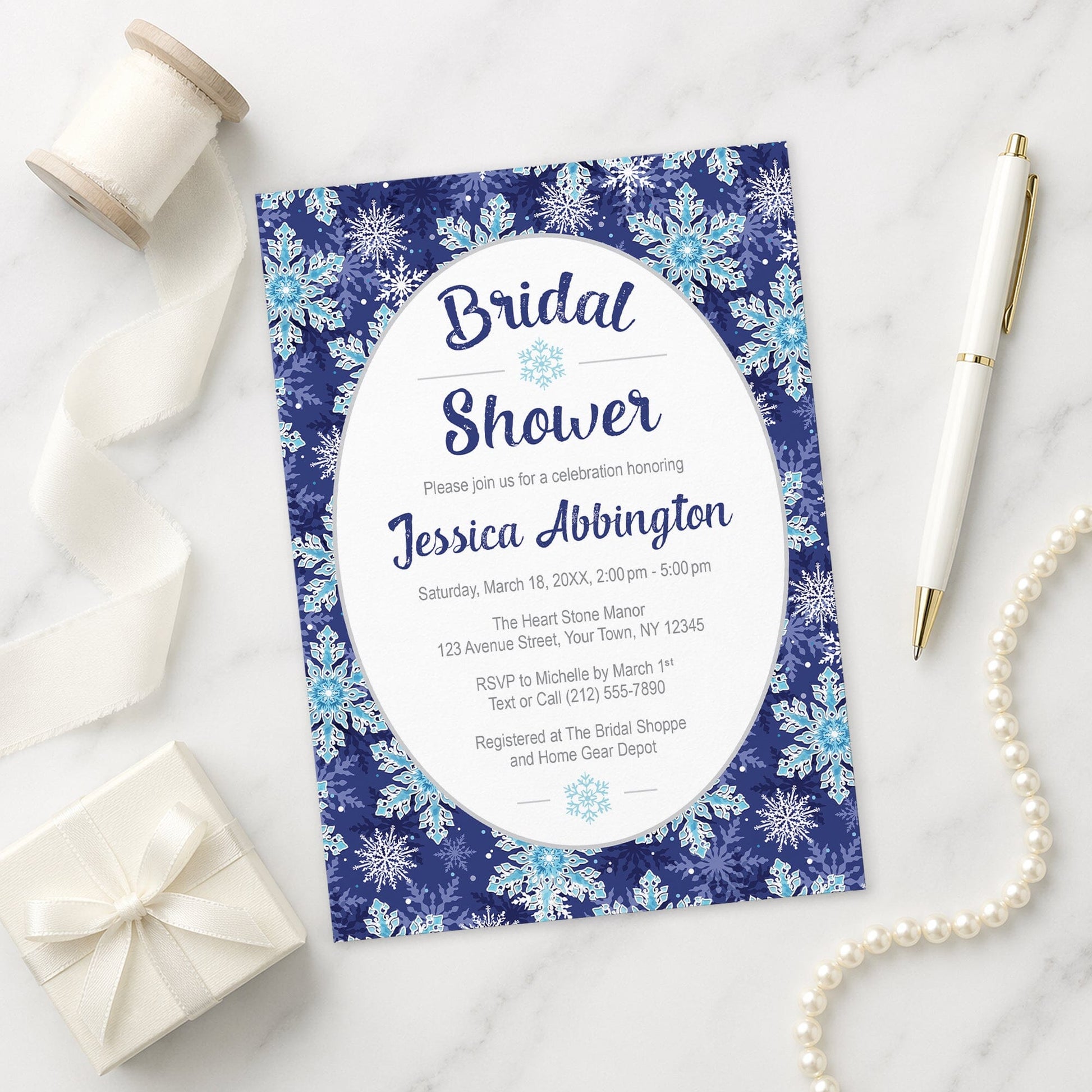 Navy Blue Snowflake Bridal Shower Invitation on a marble surface with gift, pen, and pearls.
