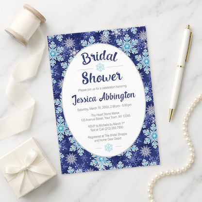 Navy Blue Snowflake Bridal Shower Invitation on a marble surface with gift, pen, and pearls.
