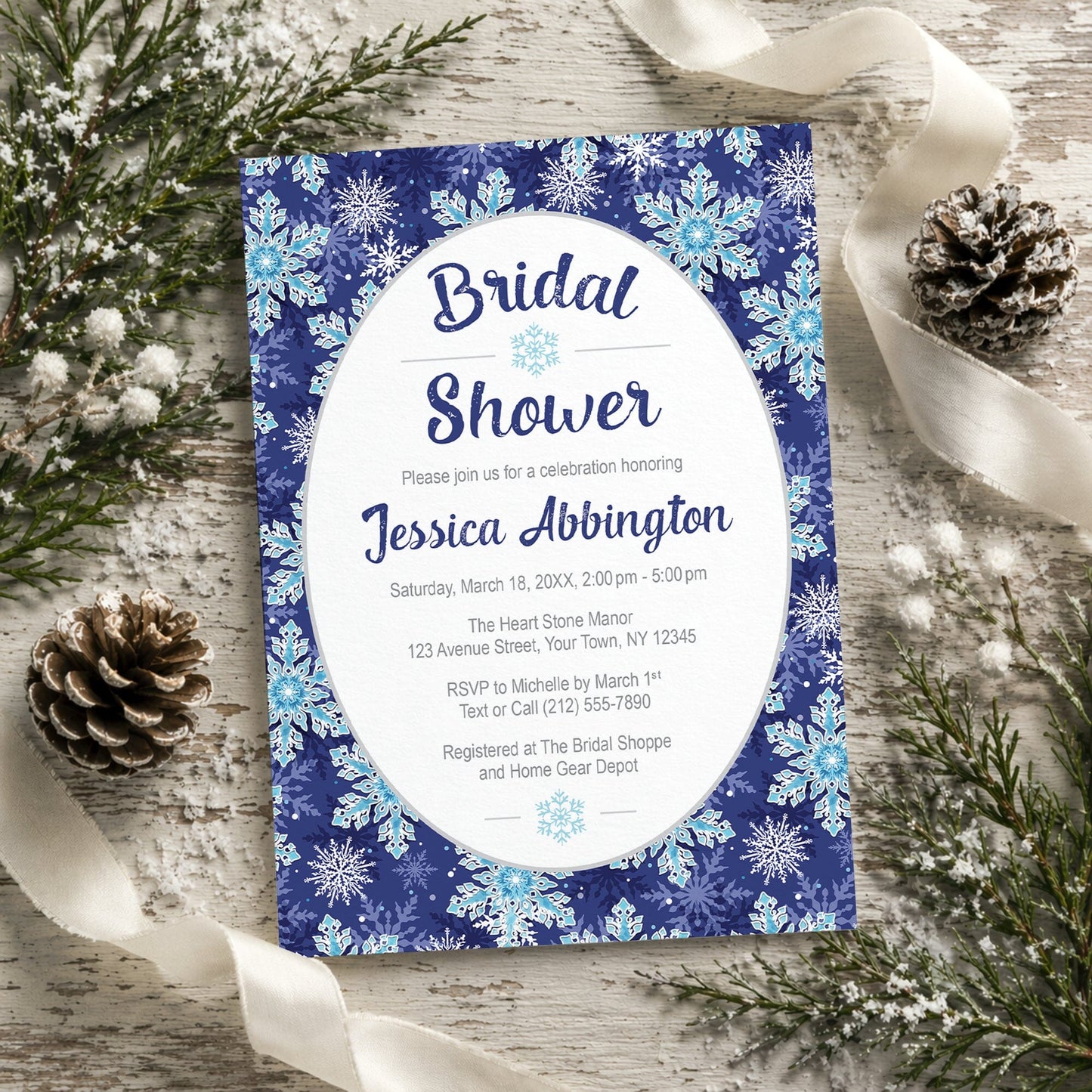 Navy Blue Snowflake Bridal Shower Invitation shown on a rustic wooden surface with winter greenery, pine cones, and ribbons.