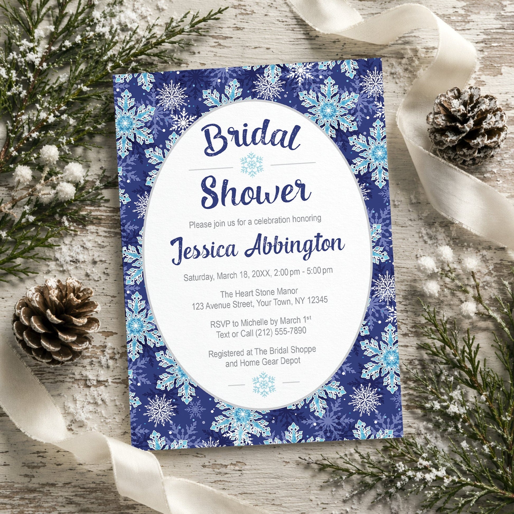 Navy Blue Snowflake Bridal Shower Invitation shown on a rustic wooden surface with winter greenery, pine cones, and ribbons.