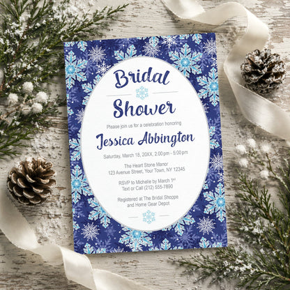 Navy Blue Snowflake Bridal Shower Invitation shown on a rustic wooden surface with winter greenery, pine cones, and ribbons.