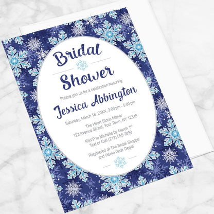 Navy Blue Snowflake Bridal Shower Invitation shown at an angle on a marble surface with a white envelope.