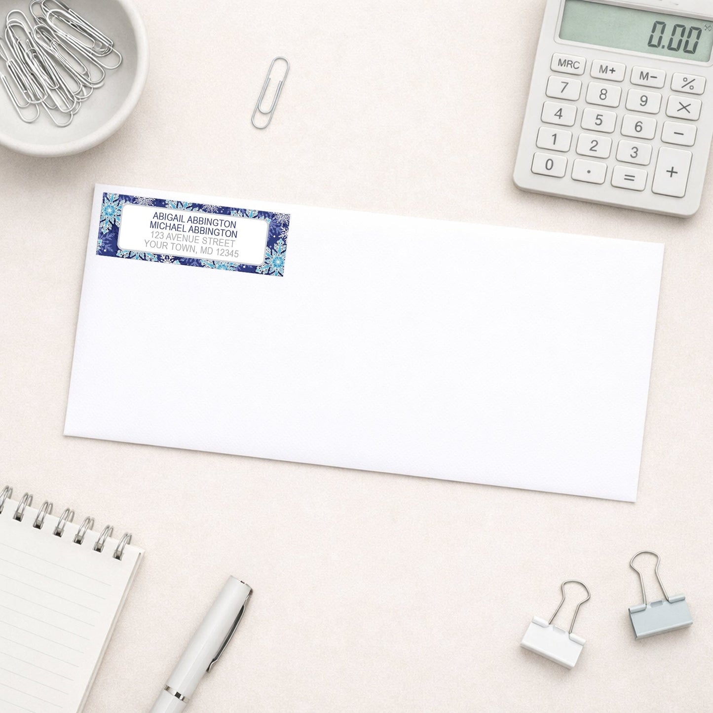 Navy Blue Snowflake Winter Return Address Label shown on a white envelope with everyday office supplies