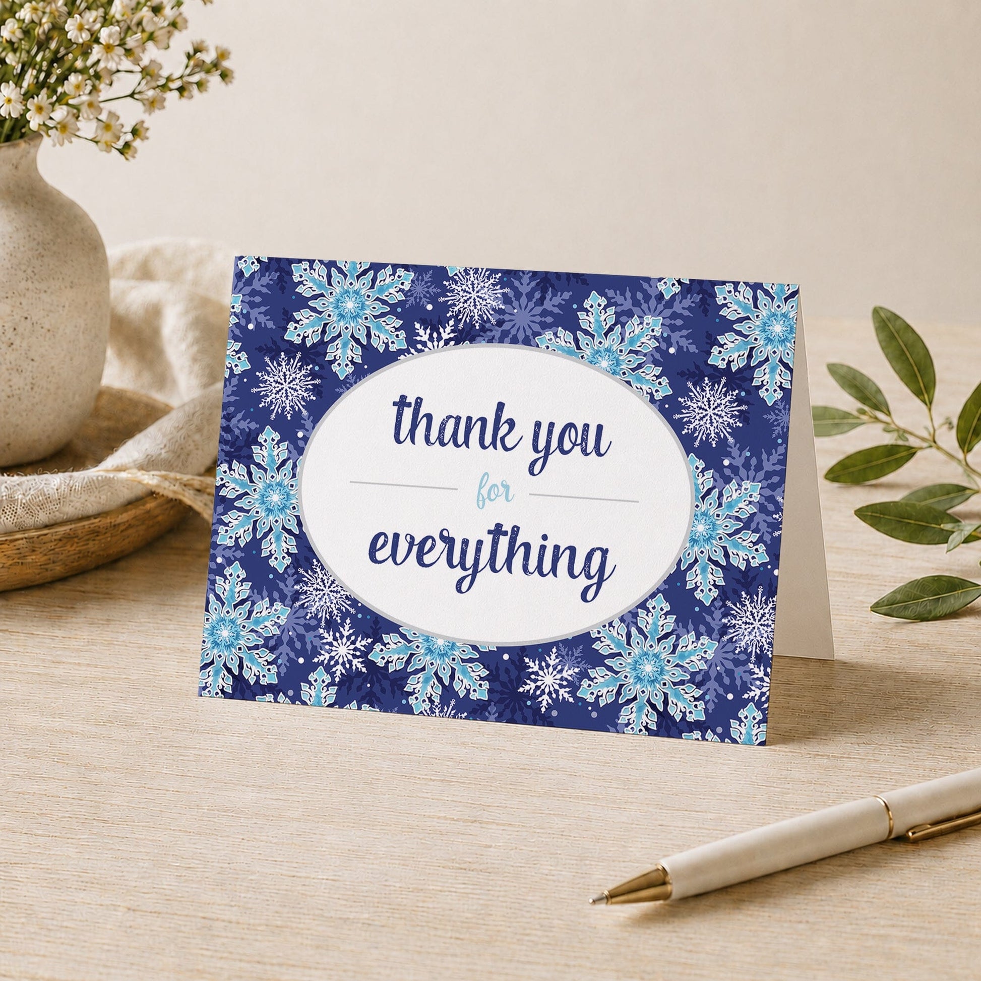 Navy Blue Snowflake Winter Thank You Card shown a desk with a vase, plants, and a pen.
