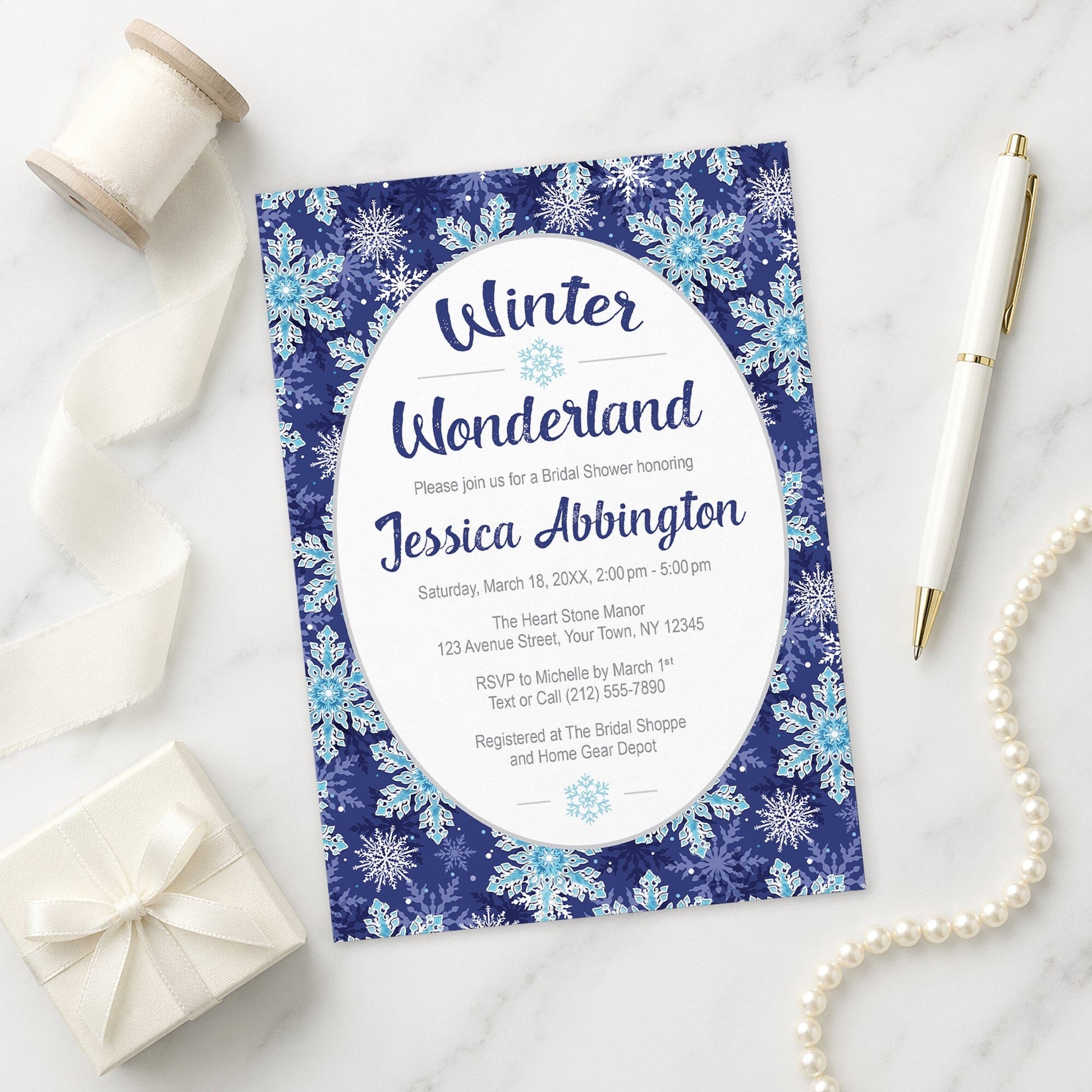 Winter Wonderland bridal shower invitation with navy blue snowflake design shown on a marble surface with decorative items.