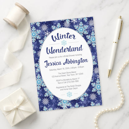 Winter Wonderland bridal shower invitation with navy blue snowflake design shown on a marble surface with decorative items.